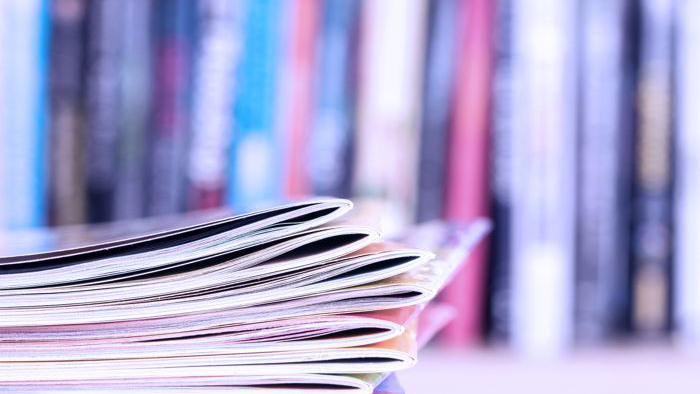 Close up edge of colorful magazine stacking with  blurry bookshelf background for publication and publishing concept .
